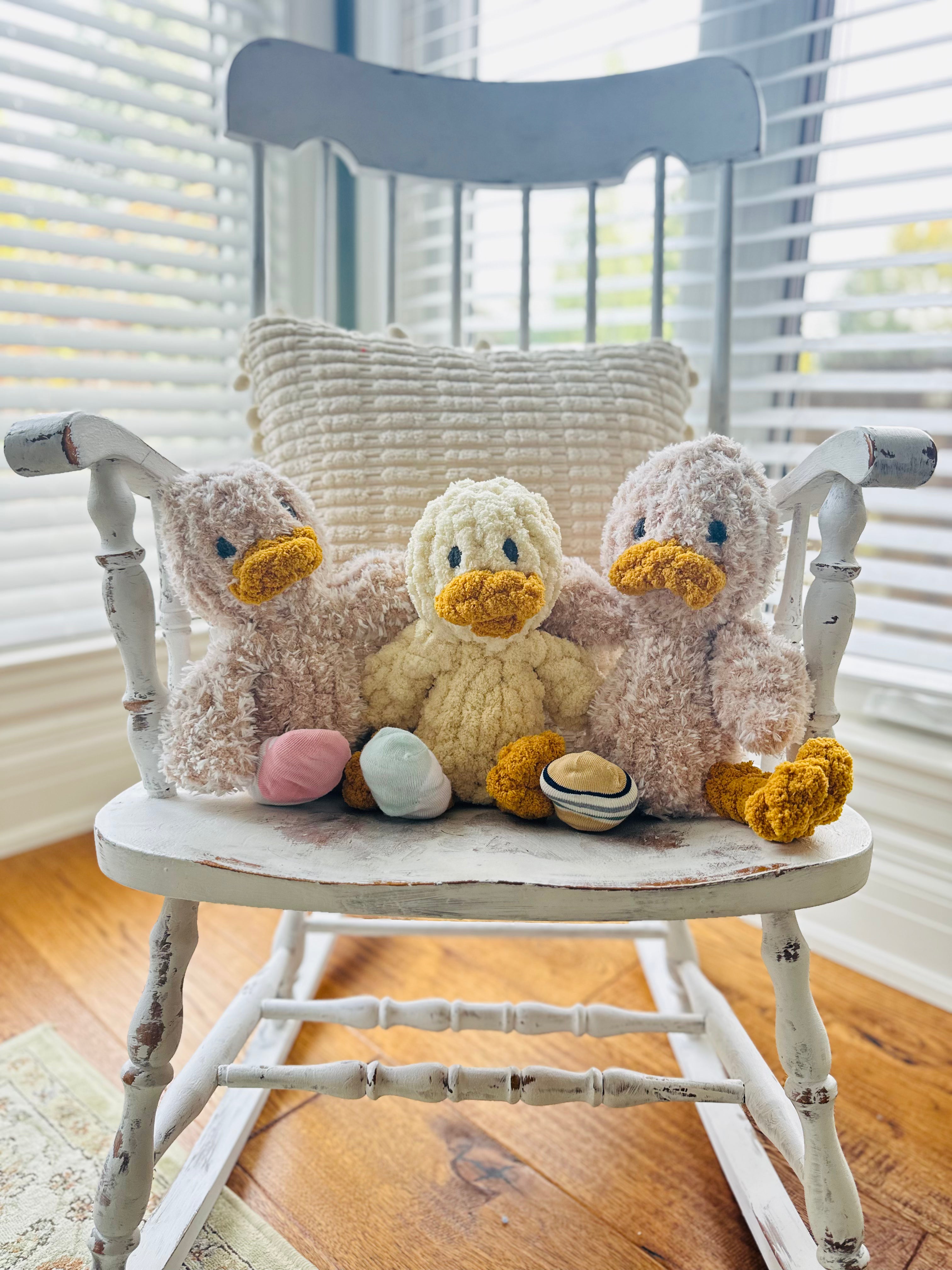 Three plush ducks on a white wooden chair with a neutral background