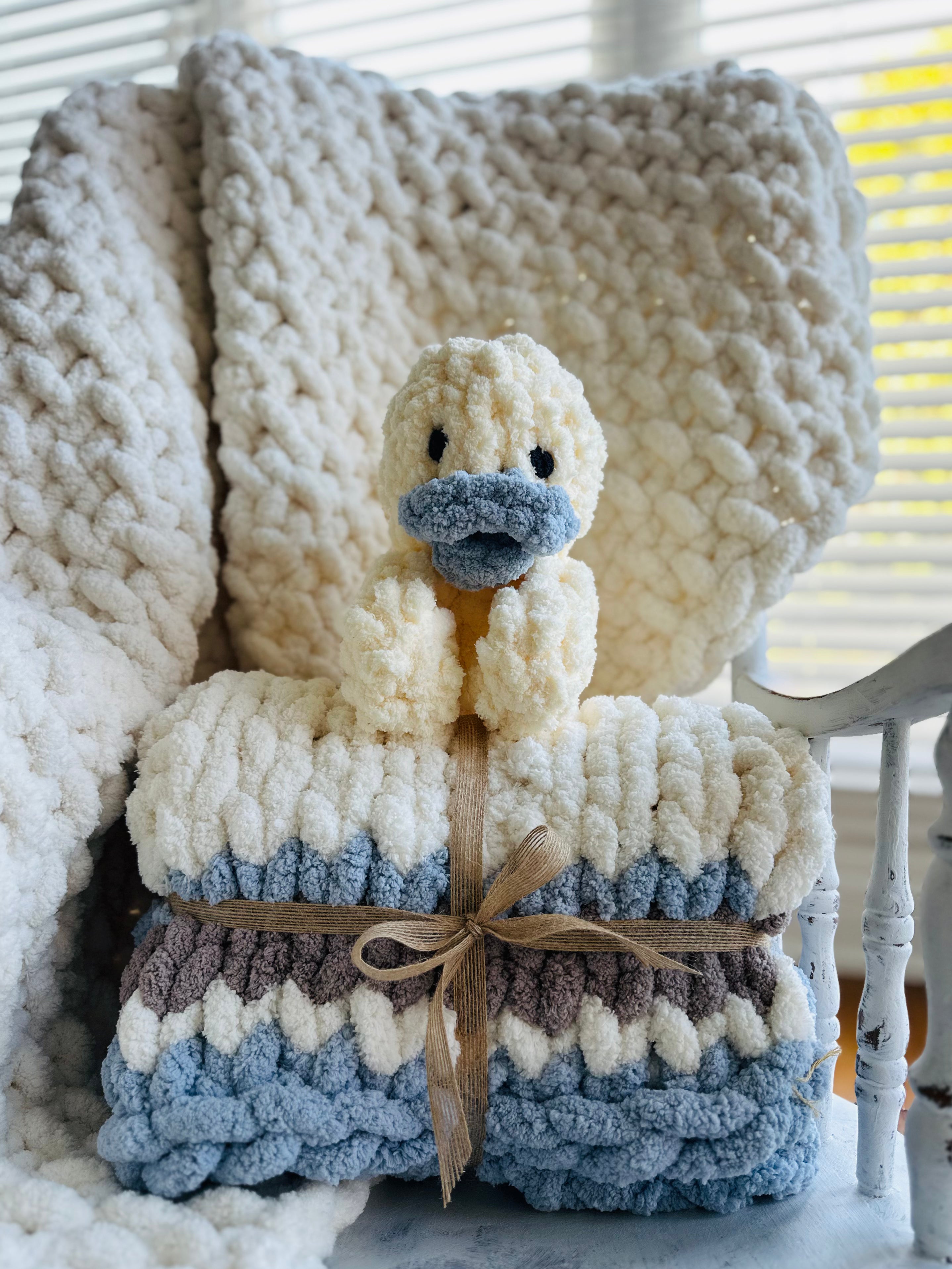 Knitted blanket with a duck-shaped toy on top, wrapped with a ribbon.